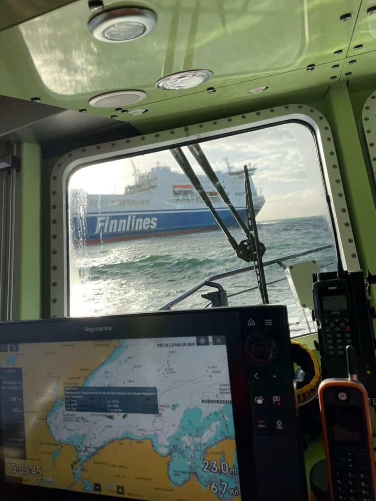 Sie sehen durch ein Bootsfenster ein Schiff der Seenotrettung.