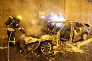 Einsatzkräfte vor einem ausgebrannten Pkw.