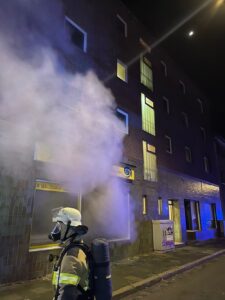 Eine Einsatzkraft mit Atemschutz vor dem verrauchten Waschsalon an der Vorderseite des Gebäudes. Foto: Feuerwehr Bremerhaven