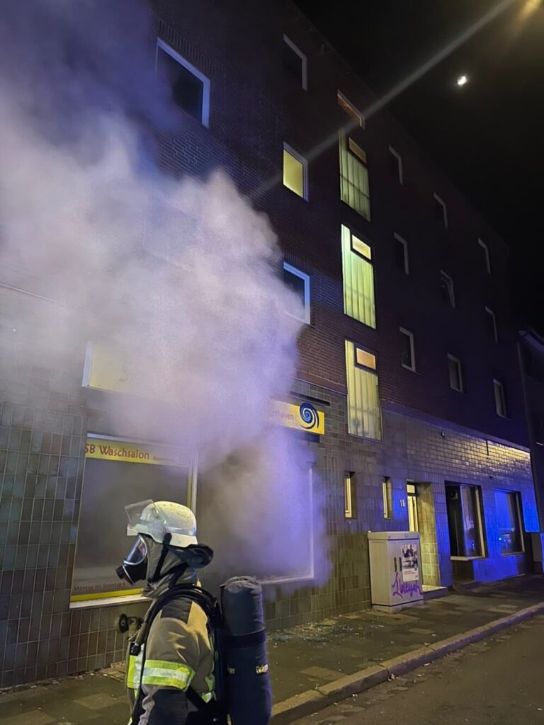 Eine Einsatzkraft mit Atemschutz vor dem verrauchten Waschsalon an der Vorderseite des Gebäudes. Foto: Feuerwehr Bremerhaven
